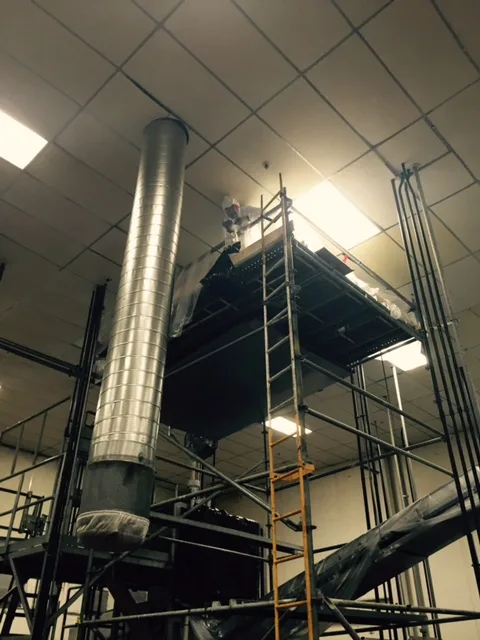A tall vertical exhaust duct inside a commercial kitchen, with a ladder beside it
