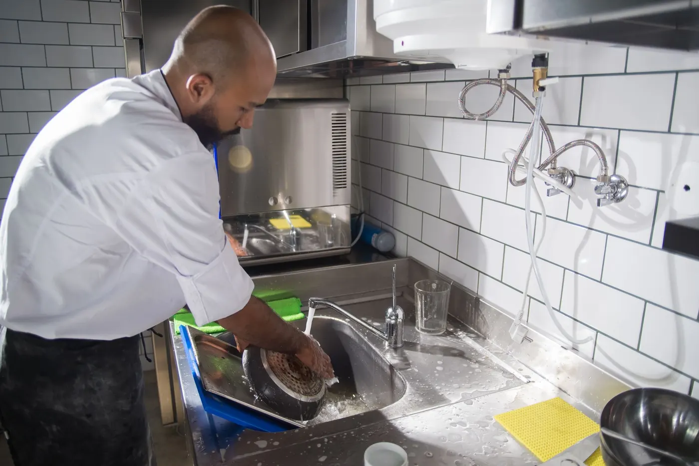 Stock photo of a cook washing up at a stainless sink in a commercial kitchen