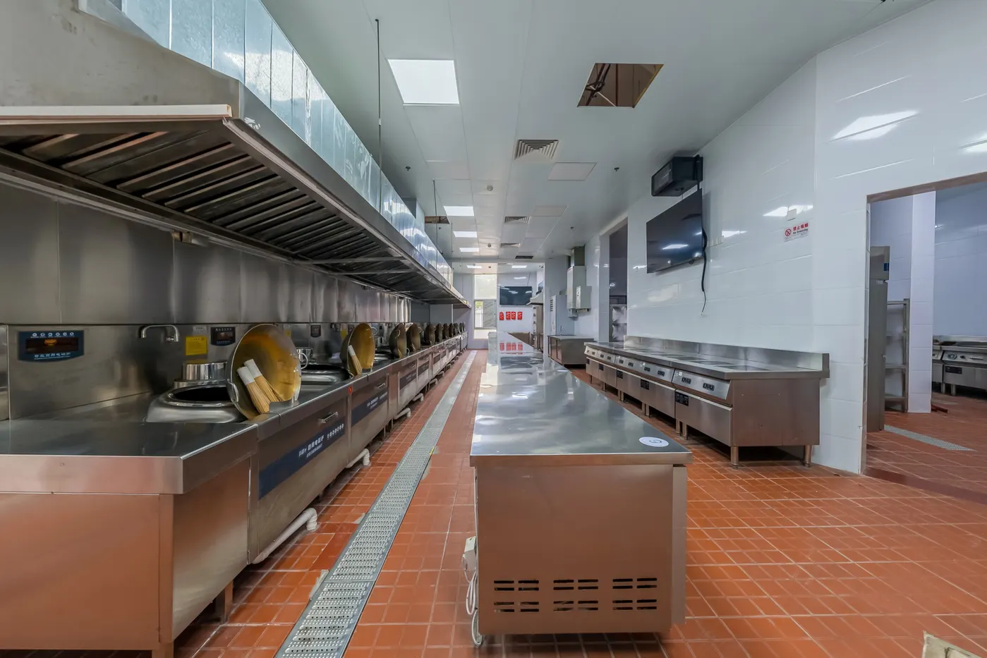 Stock photo of a long commercial kitchen line under a continuous stainless exhaust hood